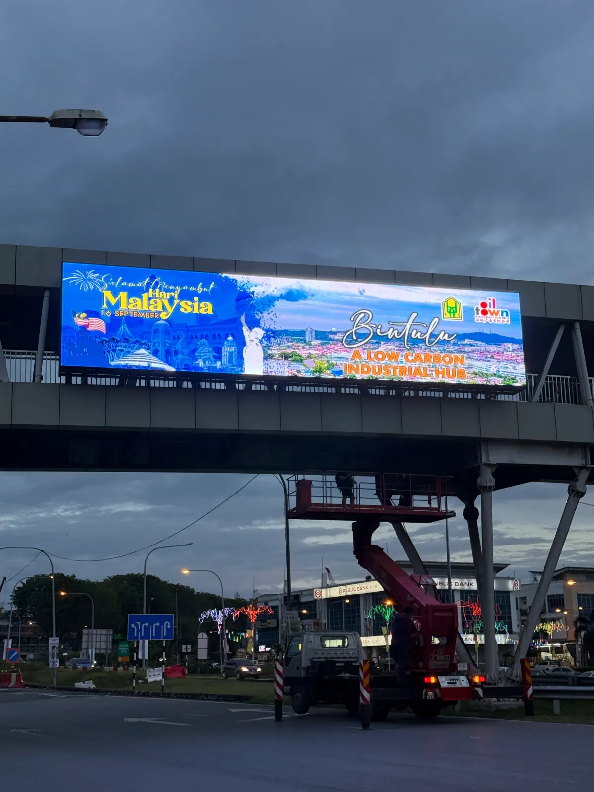 Overhead LED screen on a pedestrian bridge in Bintulu displaying a Hari Malaysia greeting
